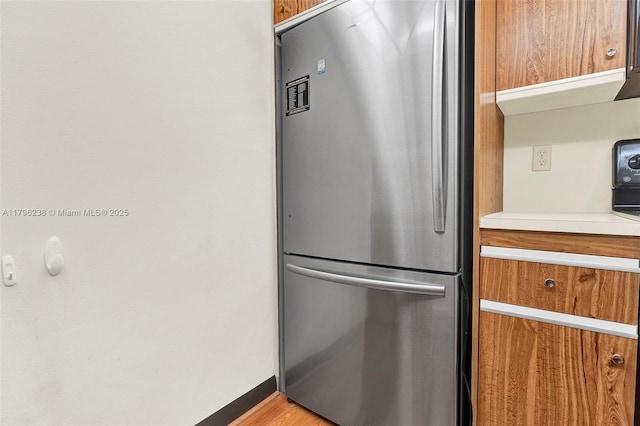 kitchen featuring light countertops, baseboards, freestanding refrigerator, and brown cabinets
