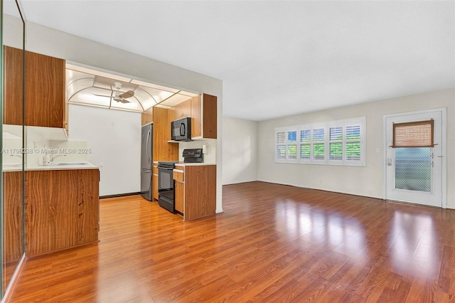 kitchen featuring light countertops, brown cabinetry, black appliances, and light wood-style flooring