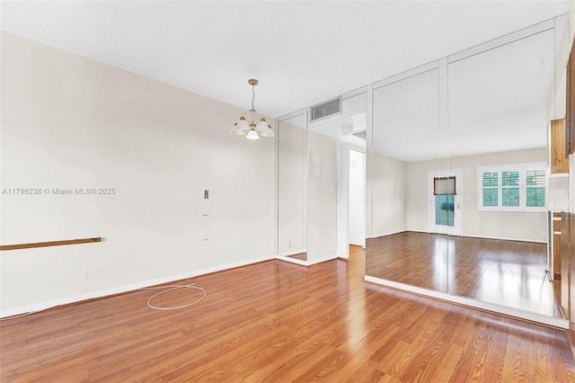 unfurnished room with visible vents, baseboards, wood finished floors, and a notable chandelier