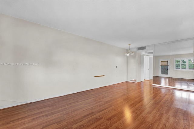 unfurnished living room featuring a notable chandelier, wood finished floors, and visible vents
