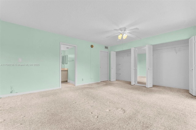 unfurnished bedroom featuring visible vents, a ceiling fan, multiple closets, ensuite bathroom, and carpet flooring