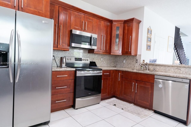 kitchen with a sink, light stone counters, glass insert cabinets, stainless steel appliances, and light tile patterned flooring