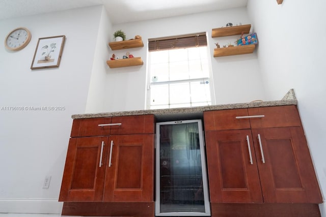 kitchen with open shelves, wine cooler, brown cabinets, and light stone countertops