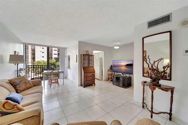 living area featuring visible vents, baseboards, a textured ceiling, expansive windows, and light tile patterned floors