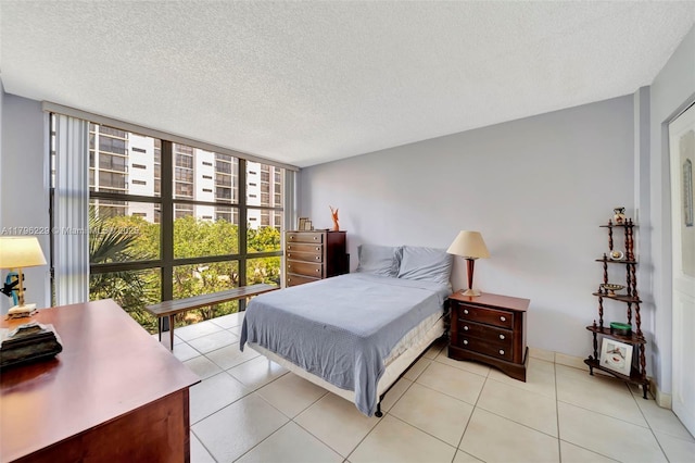 bedroom featuring a wall of windows, light tile patterned floors, and a textured ceiling