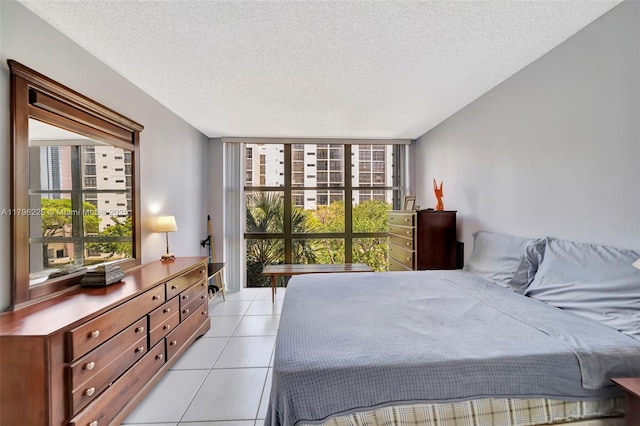 bedroom with a textured ceiling, a wall of windows, multiple windows, and light tile patterned floors