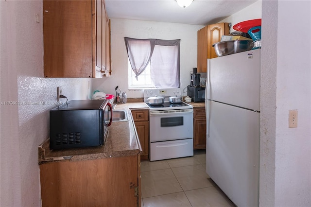 kitchen with light tile patterned floors, brown cabinets, a textured wall, and white appliances