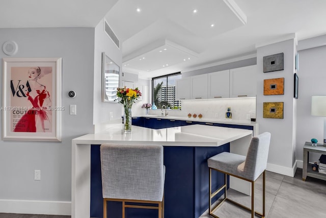kitchen featuring light countertops, baseboards, white cabinets, a breakfast bar, and recessed lighting