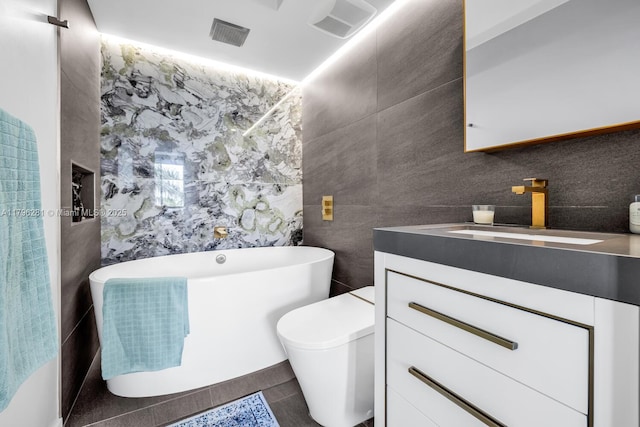 full bathroom with vanity, visible vents, a freestanding tub, toilet, and tile walls