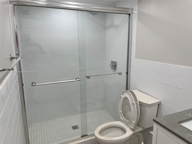 bathroom with vanity, a stall shower, toilet, and tile walls