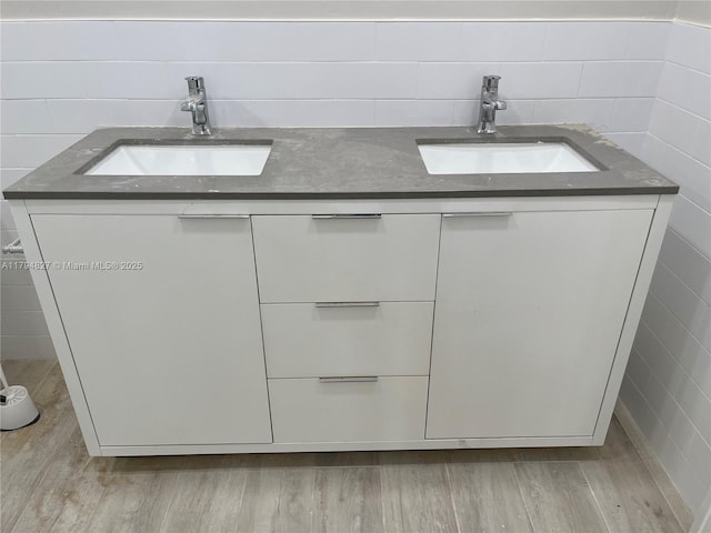 bathroom with double vanity, tile walls, a sink, and wood finished floors