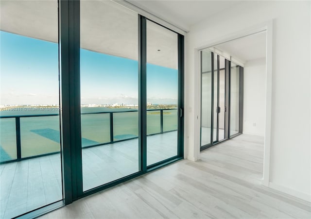 spare room with expansive windows, a water view, and wood finished floors