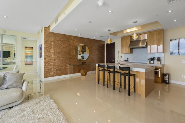 kitchen with brown cabinets, baseboards, open floor plan, wall chimney exhaust hood, and oven