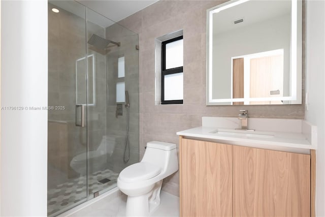 bathroom with visible vents, tile walls, a stall shower, vanity, and toilet