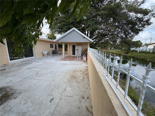 exterior space featuring central AC unit, a patio, fence, a water view, and stucco siding