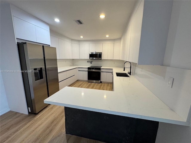 kitchen featuring appliances with stainless steel finishes, a sink, light wood-style flooring, a peninsula, and visible vents