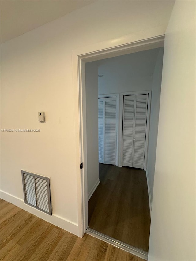 hall with baseboards, visible vents, and wood finished floors
