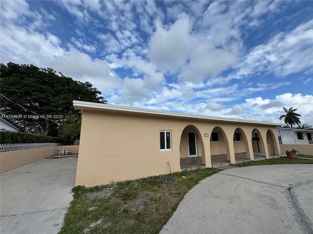 view of front facade featuring covered porch, fence, driveway, and stucco siding