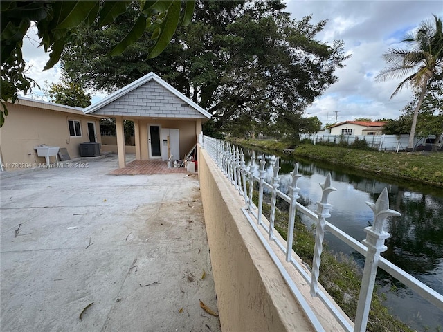 exterior space with fence, a water view, and central AC