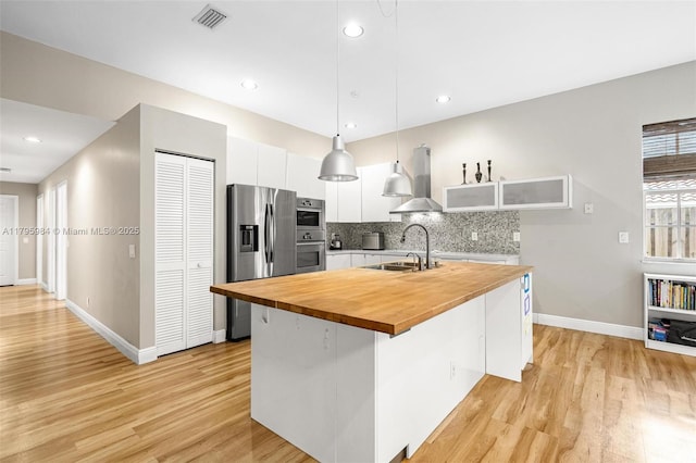 kitchen with butcher block countertops, visible vents, ventilation hood, stainless steel appliances, and white cabinets