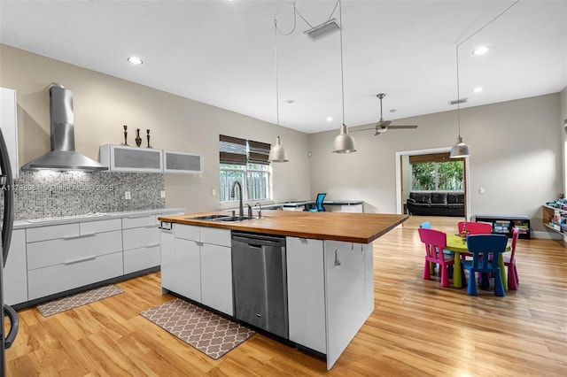 kitchen featuring a sink, a healthy amount of sunlight, butcher block countertops, wall chimney range hood, and dishwasher