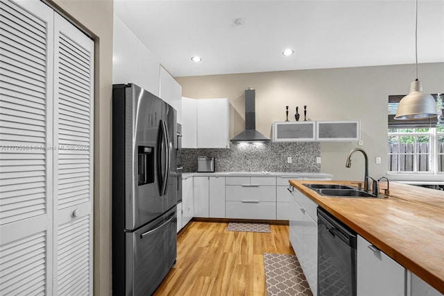 kitchen featuring dishwashing machine, wooden counters, a sink, stainless steel refrigerator with ice dispenser, and wall chimney range hood