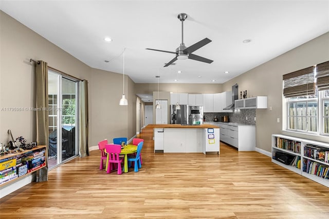 kitchen featuring butcher block counters, stainless steel refrigerator with ice dispenser, wall chimney exhaust hood, white cabinetry, and light wood-style floors