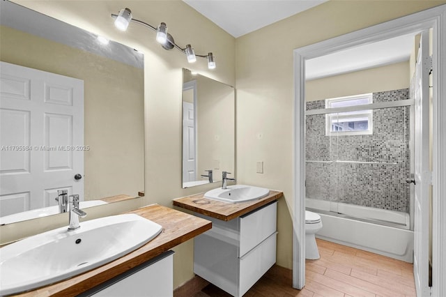 bathroom featuring a sink, toilet, two vanities, and shower / bath combination with glass door