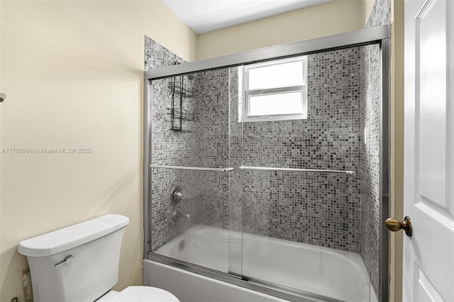 bathroom with toilet and shower / bath combination with glass door