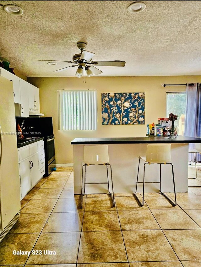 5706 Simms St, Hollywood, FL 33021 - kitchen with freestanding refrigerator, white cabinets, a textured ceiling, ceiling fan, and dark countertops