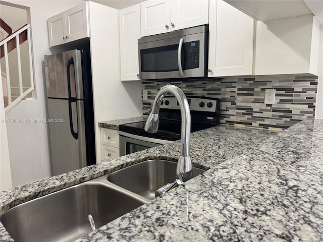 kitchen with appliances with stainless steel finishes, tasteful backsplash, light stone countertops, a sink, and white cabinets