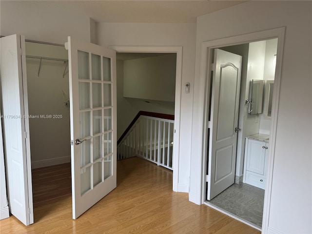 hallway with baseboards, french doors, and light wood-type flooring
