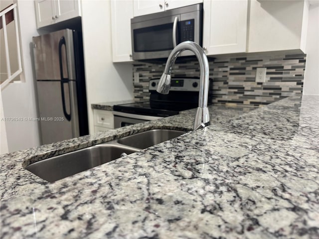 kitchen with white cabinets, backsplash, light stone countertops, and appliances with stainless steel finishes