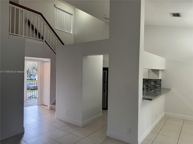 interior space featuring stairway, a high ceiling, light tile patterned flooring, and visible vents
