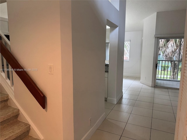 corridor featuring a healthy amount of sunlight, baseboards, stairs, and light tile patterned flooring