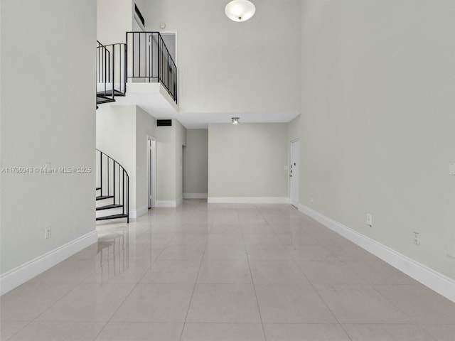unfurnished living room with stairway, light tile patterned floors, a high ceiling, and baseboards