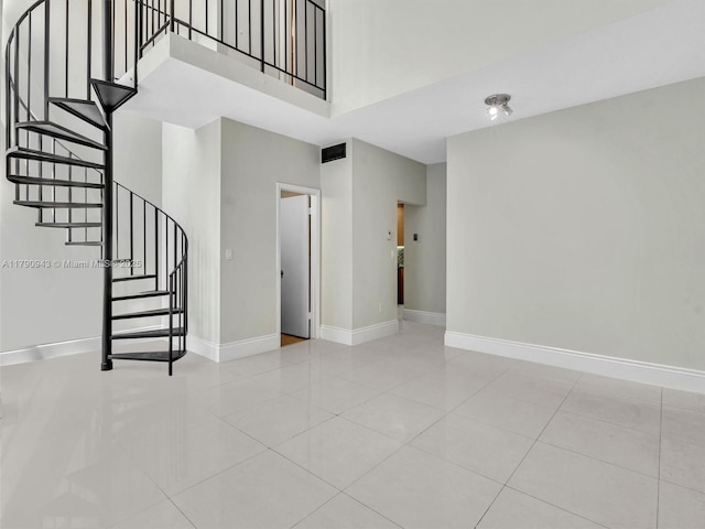 unfurnished living room featuring baseboards, a towering ceiling, tile patterned flooring, and stairway