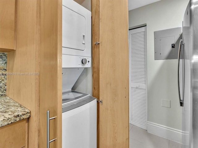 laundry room featuring laundry area, stacked washing maching and dryer, light tile patterned floors, and electric panel