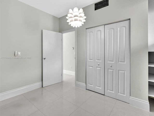 unfurnished bedroom featuring visible vents, baseboards, a closet, an inviting chandelier, and light tile patterned flooring