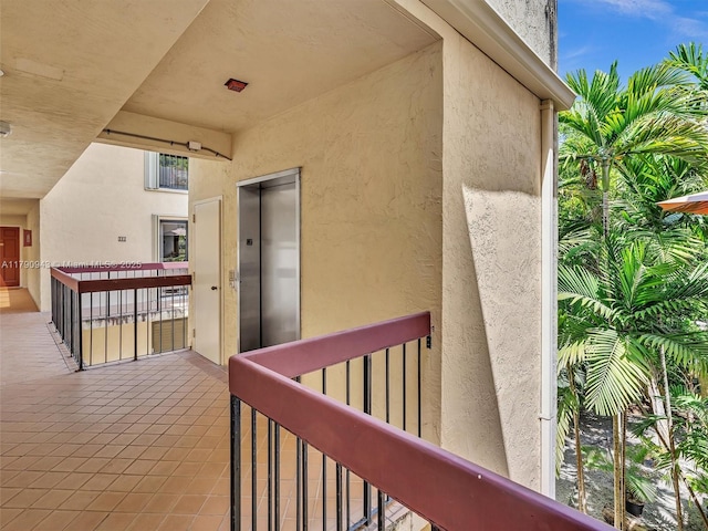 view of exterior entry with stucco siding, elevator, and a balcony