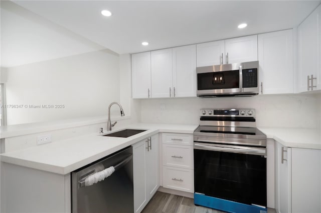 kitchen with a peninsula, a sink, stainless steel appliances, white cabinets, and light countertops