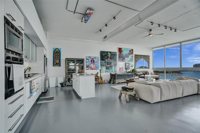 living area with a ceiling fan, finished concrete floors, expansive windows, track lighting, and a water view