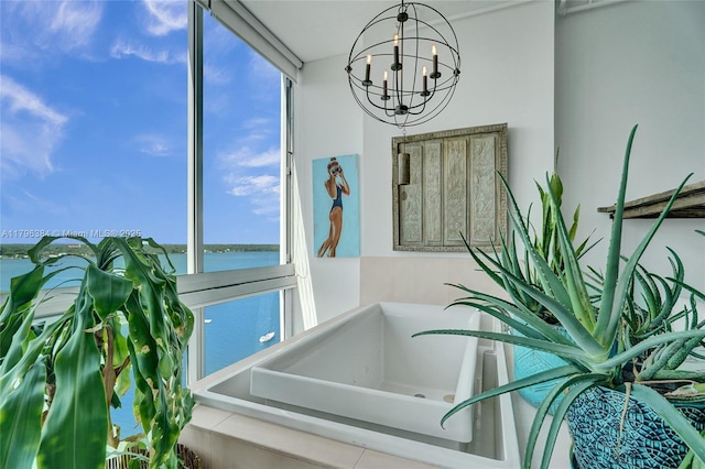 bathroom with a tub, a water view, a notable chandelier, and a wealth of natural light