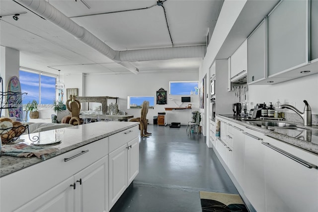 kitchen with concrete flooring, a sink, white cabinets, open floor plan, and stainless steel appliances
