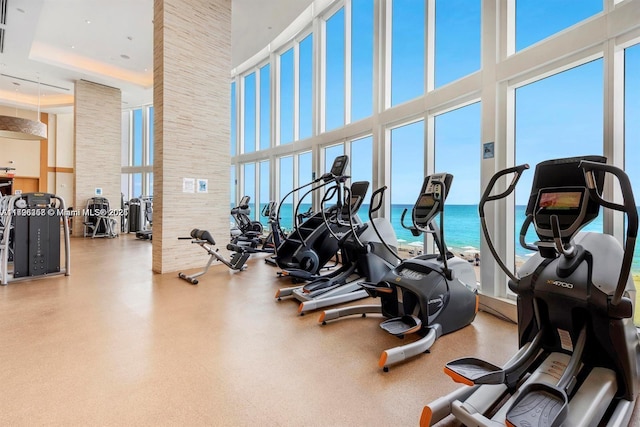 exercise room featuring a towering ceiling and a water view