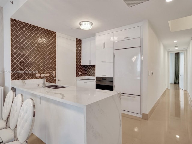 kitchen with a sink, white built in fridge, wall oven, and white cabinets
