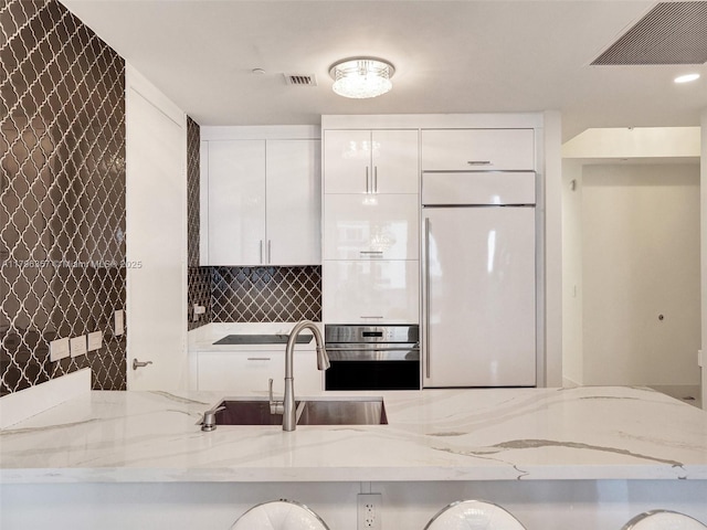 kitchen with built in refrigerator, a sink, oven, and white cabinetry
