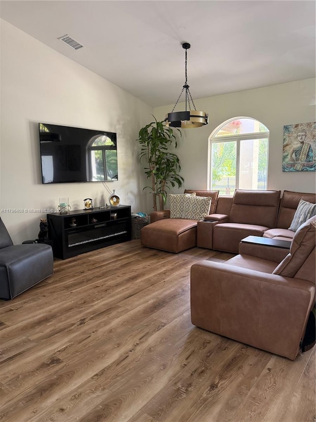 living area featuring visible vents, wood finished floors, vaulted ceiling, and a healthy amount of sunlight