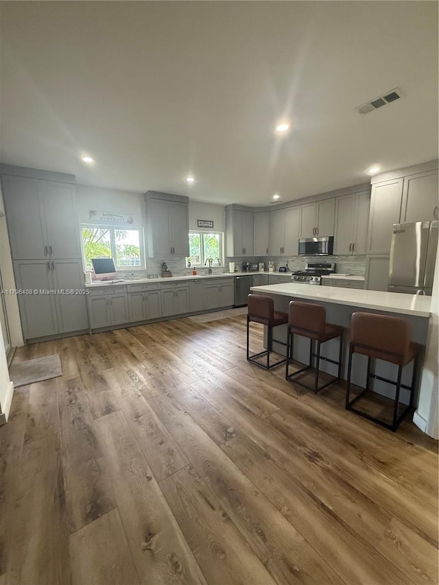 kitchen featuring visible vents, decorative backsplash, a kitchen breakfast bar, gray cabinets, and appliances with stainless steel finishes