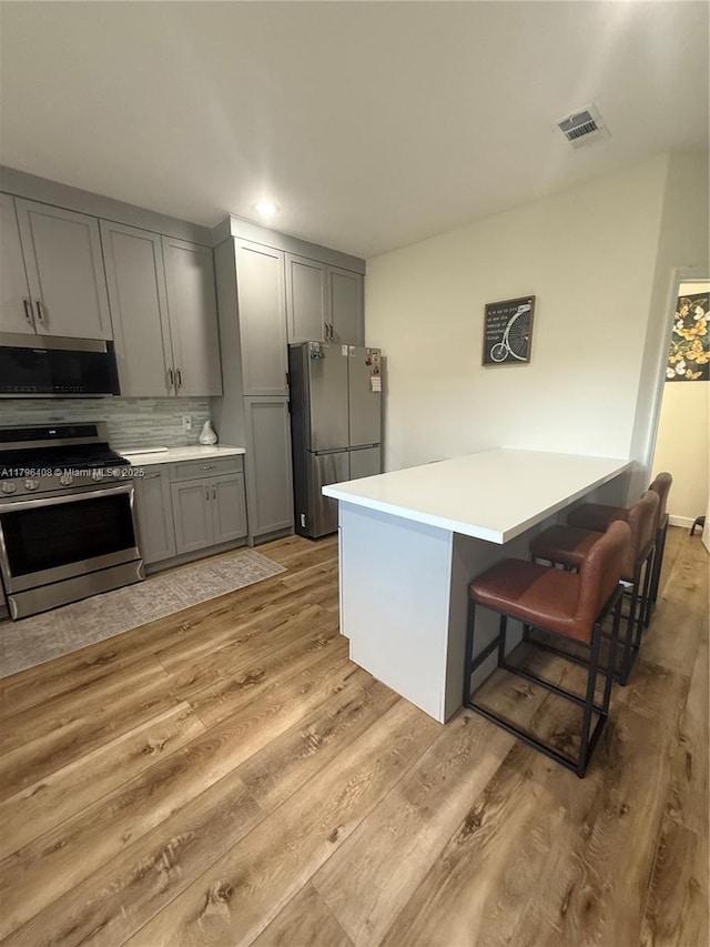 kitchen featuring gray cabinets, a kitchen bar, light wood-type flooring, light countertops, and stainless steel appliances